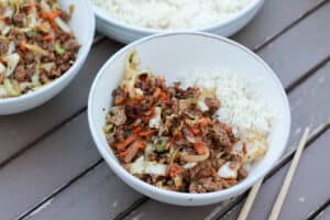 White bowl on table with beef and cabbage stir fry and rice.