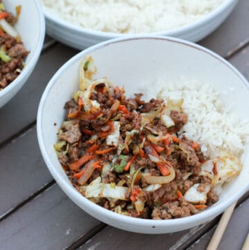 White bowl on table with beef and cabbage stir fry and rice.