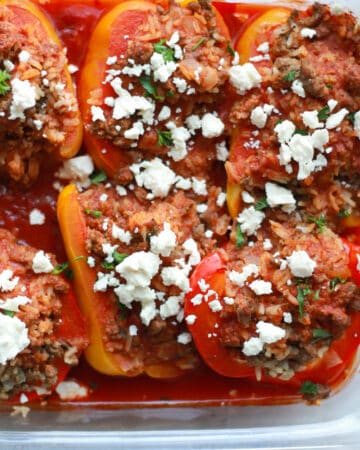 Cooked stuffed peppers in glass dish with feta cheese topping.
