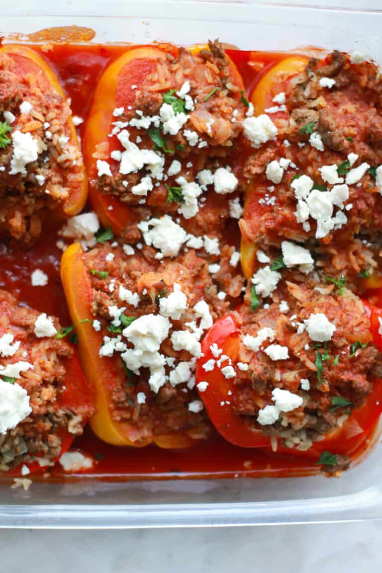 Cooked stuffed peppers in glass dish with feta cheese topping.
