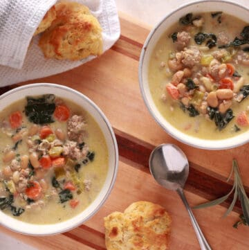 Tuscan white bean soup with biscuits on a cutting board.
